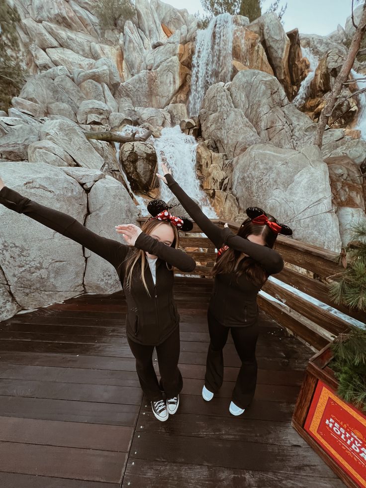 two women are standing in front of a waterfall with their arms stretched out to the side