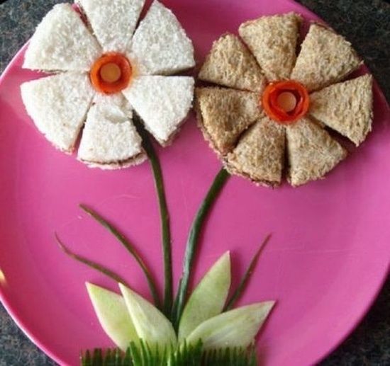 a pink plate topped with two flowers and small sandwiches on top of eachother