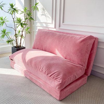 a pink couch sitting on top of a rug next to a potted plant