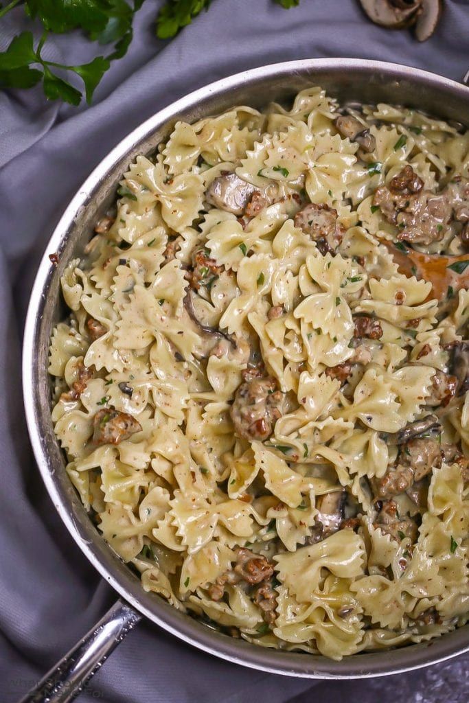 a pan filled with pasta and mushrooms on top of a blue cloth next to silverware