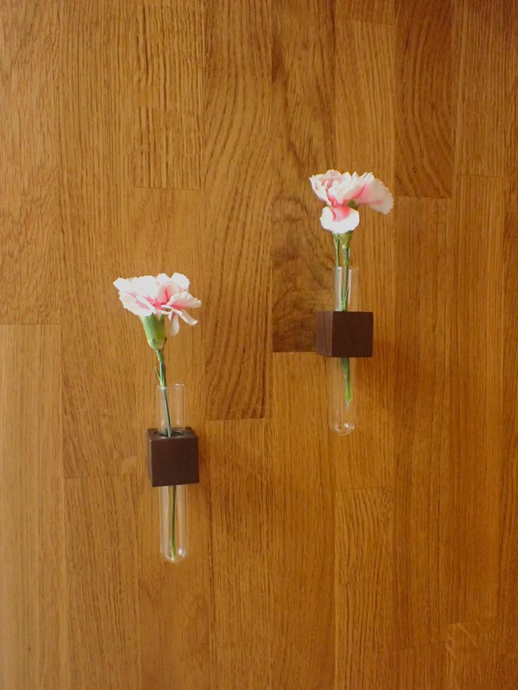 two glass vases with flowers in them on a wooden wall next to each other