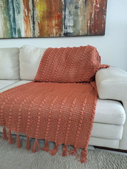 an orange crocheted afghan draped over a white couch in front of a painting