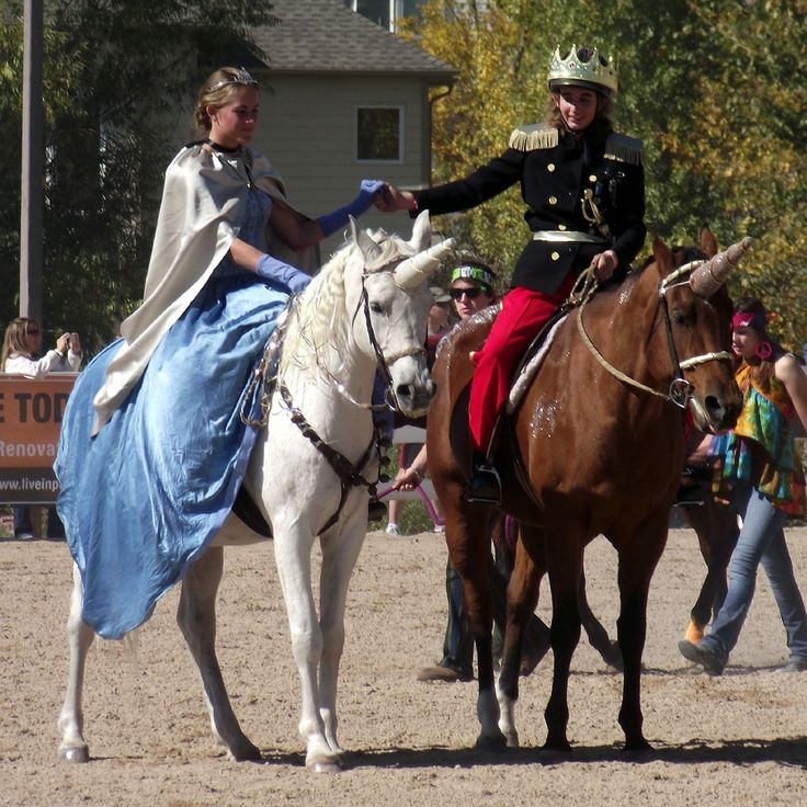 two women dressed as princesses riding on horses in front of a group of people