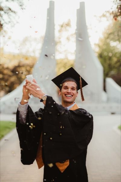 a man in graduation cap and gown throwing confetti into the air with his hands