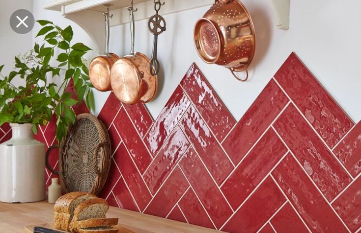 a kitchen with red tiles and copper pots on the wall next to a cutting board