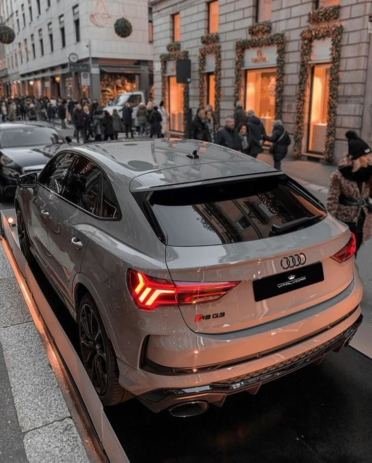 an audi car is parked on the street in front of a building with people walking by