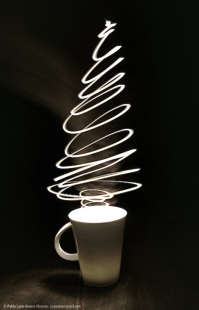 a white coffee cup sitting on top of a table next to a lit christmas tree