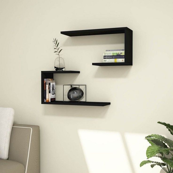 two black floating shelves in the corner of a room next to a couch and potted plant