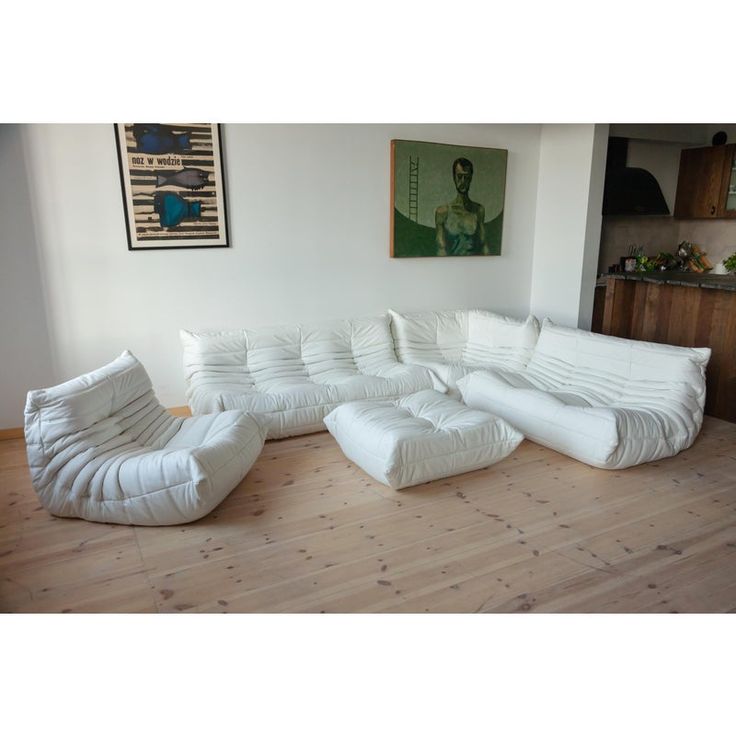 a large white couch sitting on top of a hard wood floor next to a painting