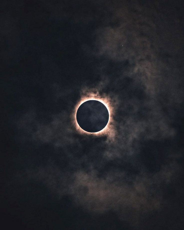 the moon is seen in front of a cloud filled sky during a partial solar eclipse