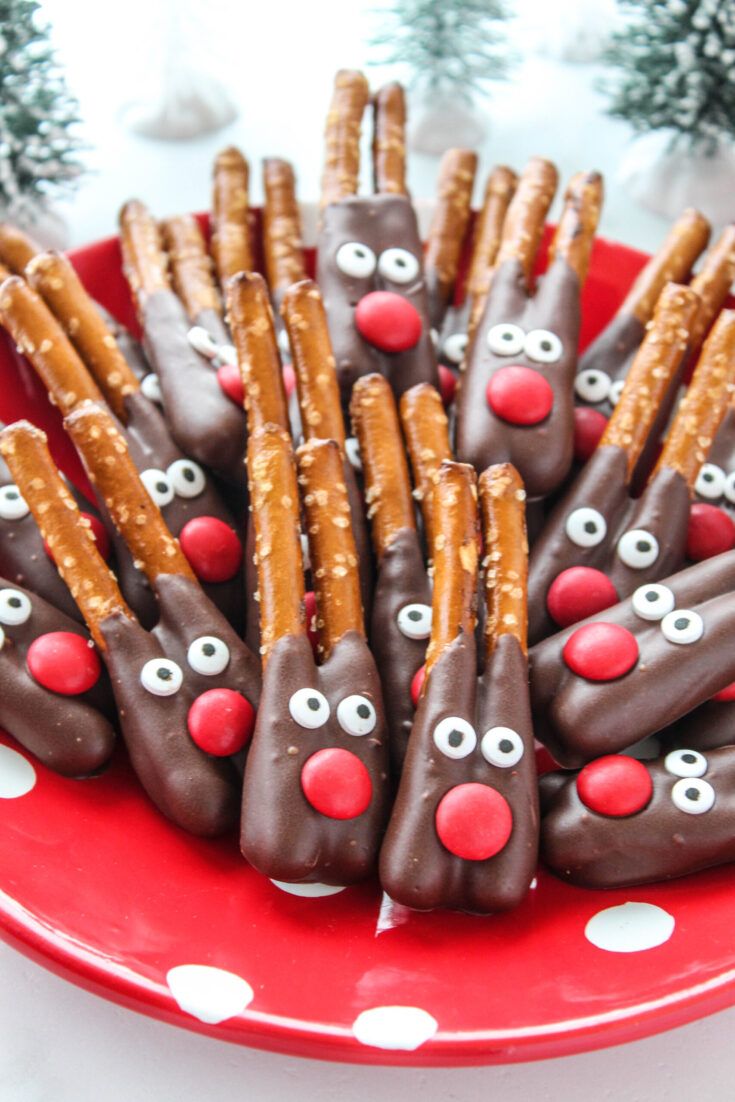 a red plate topped with pretzels covered in chocolate and reindeer noses next to christmas trees