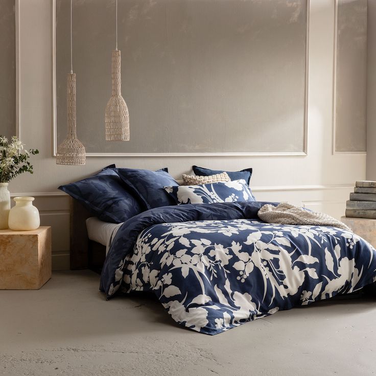 a bed with blue and white comforters in a bedroom next to a vase filled with flowers