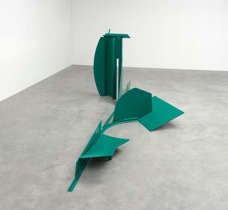 two green sculptures in an empty room with concrete flooring and white walls, one is upside down