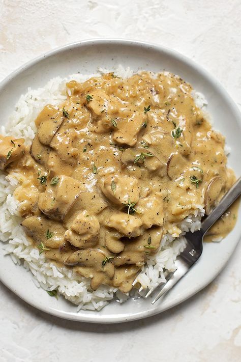 a white plate topped with rice and meat covered in gravy next to a fork