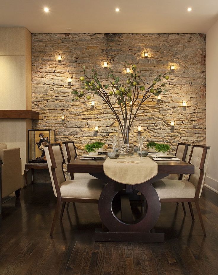 a dining room table and chairs with lights on the wall behind it in front of a stone wall