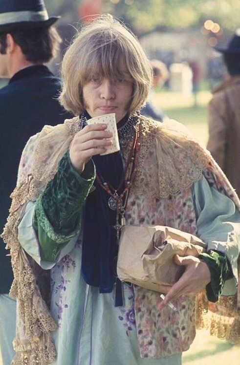 a woman with long blonde hair drinking from a paper cup while standing in front of other people