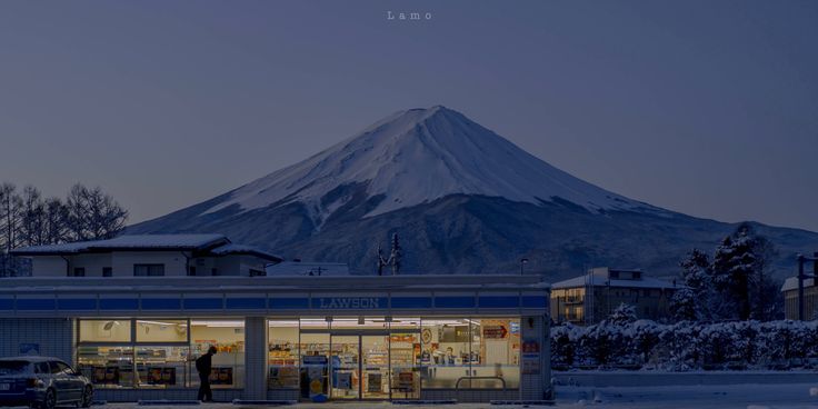 a snow covered mountain is in the distance behind a small store with cars parked outside