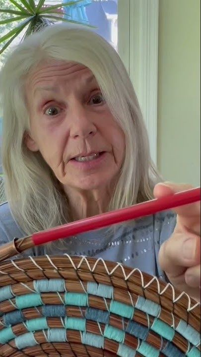 an older woman holding a woven basket in front of her face and looking at the camera