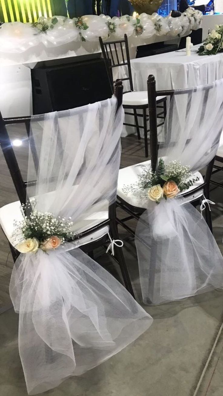 two chairs covered in white tulle with flowers and ribbons on the back, sitting next to each other