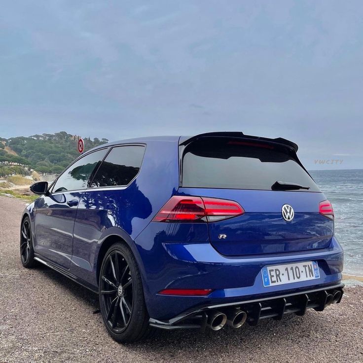 the rear end of a blue volkswagen golf gtr parked at the beach with water in the background