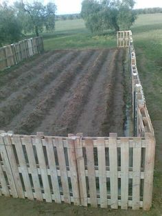 there is a wooden fence in the middle of a field with dirt and grass behind it