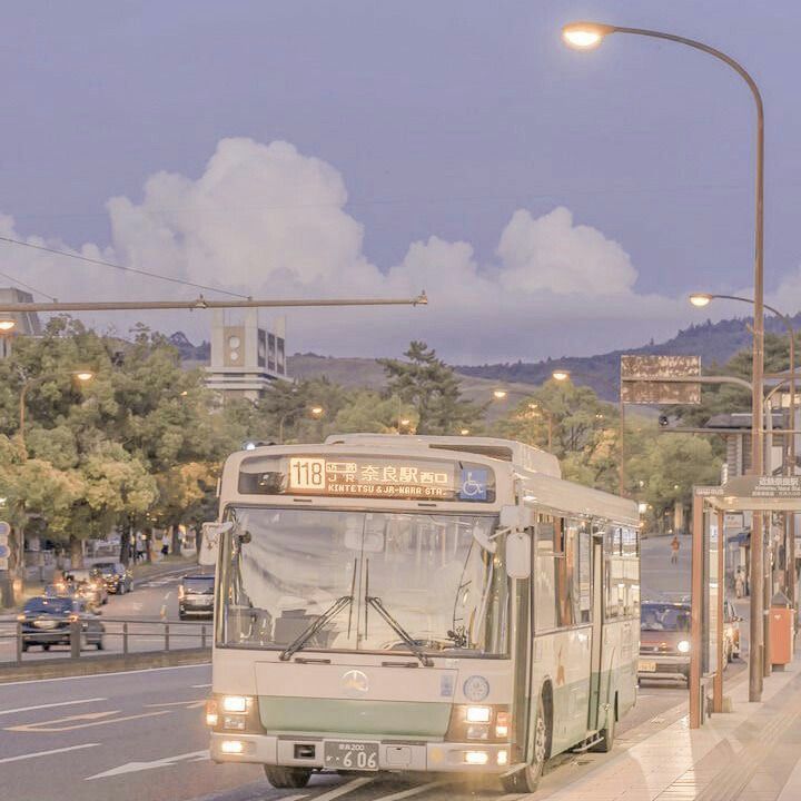 a city bus driving down the street at night with its lights on and people waiting to board