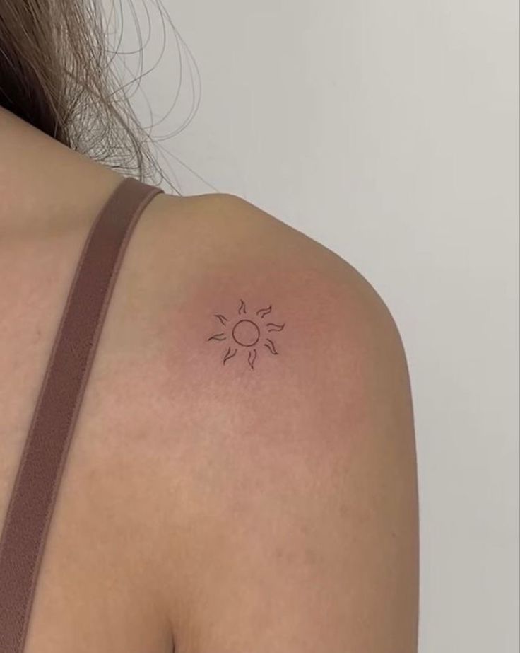 the back of a woman's shoulder with a small sun tattoo on it