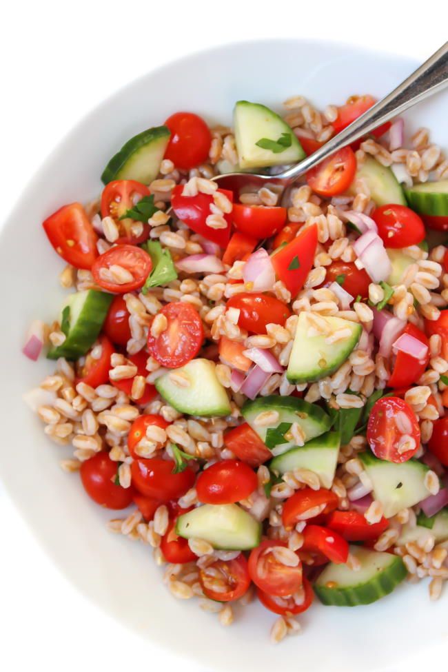 a white bowl filled with rice, cucumber and tomato salad next to a fork