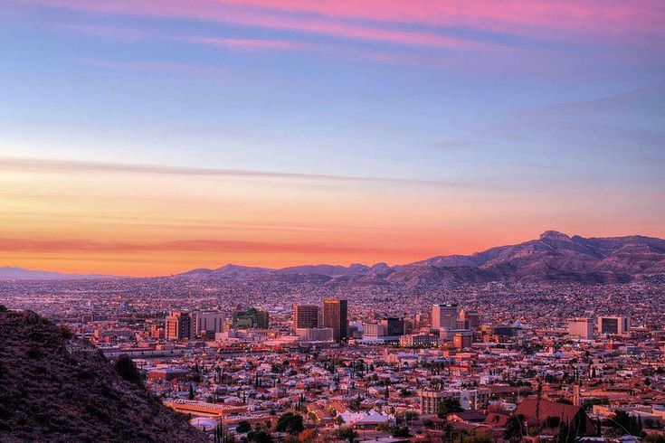 the sun is setting over a city with mountains in the backgrouund and pink sky