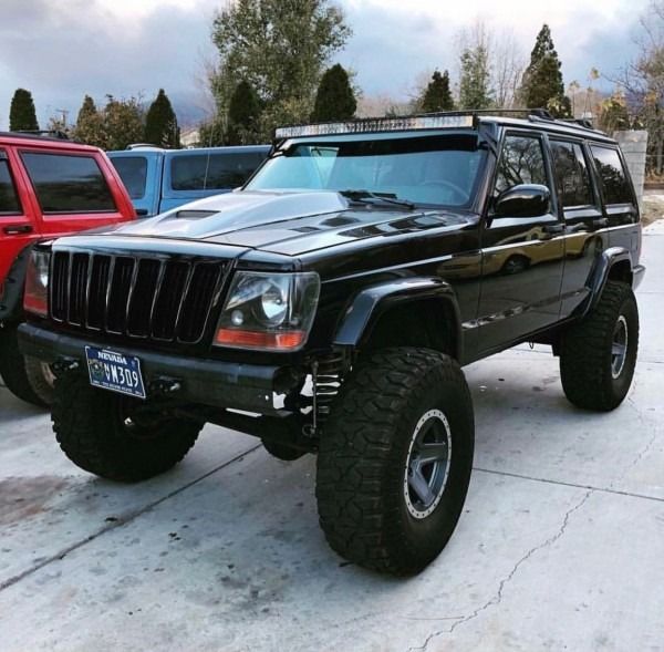 a black jeep parked in a parking lot next to another red truck and some trees