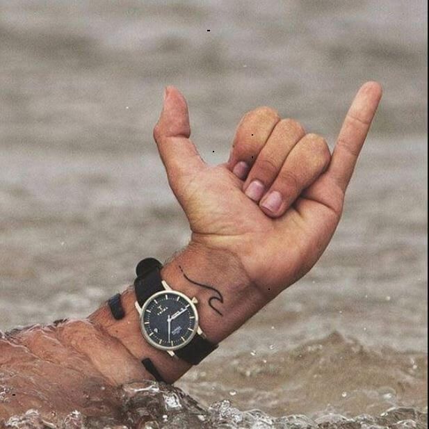 a man with a wrist tattoo holding his hand up in the water while wearing a watch