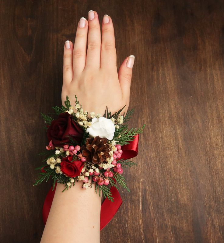 a woman's hand wearing a red and white wrist corsage on top of a wooden table