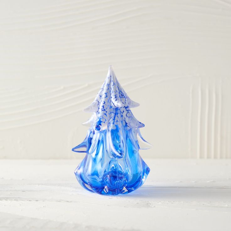 a blue glass christmas tree sitting on top of a white table next to a wall