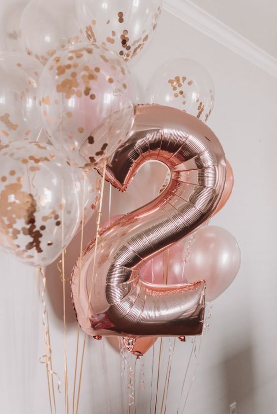 the number 2 balloon is in front of some gold and white balloons with streamers