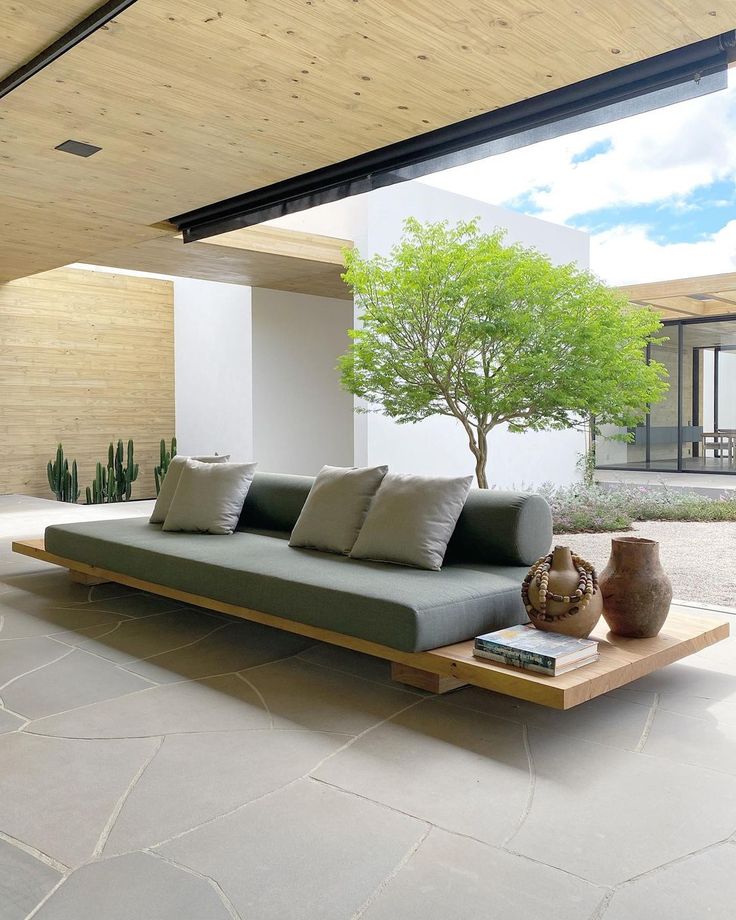 a couch sitting on top of a stone floor next to a tree and potted plant