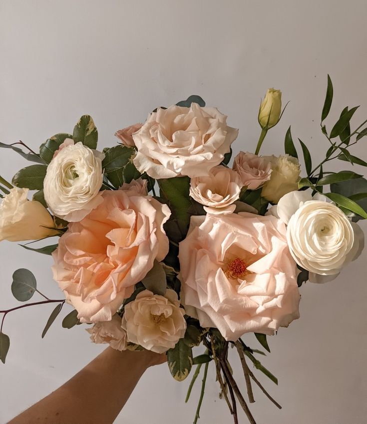 a hand holding a bouquet of flowers on a white background with greenery in the foreground