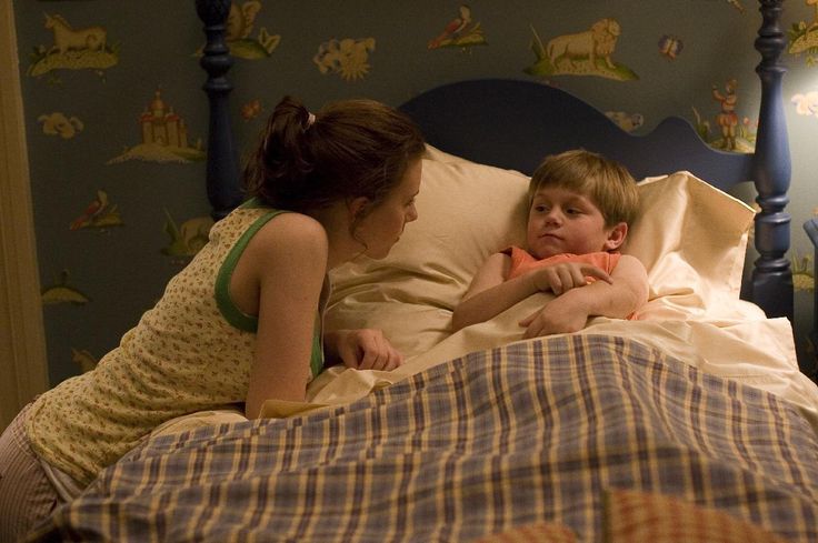 a little boy laying in bed next to a woman with her arm around his chest