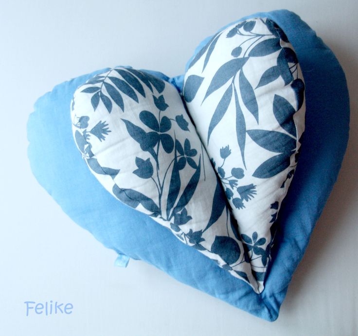 two blue and white heart shaped pillows sitting on top of a pillow that has leaves printed on it