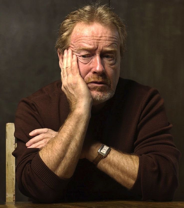 an older man sitting at a table with his hands on his face and looking off to the side