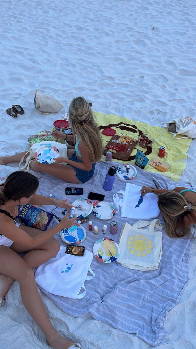 three women sitting on the beach eating and drinking