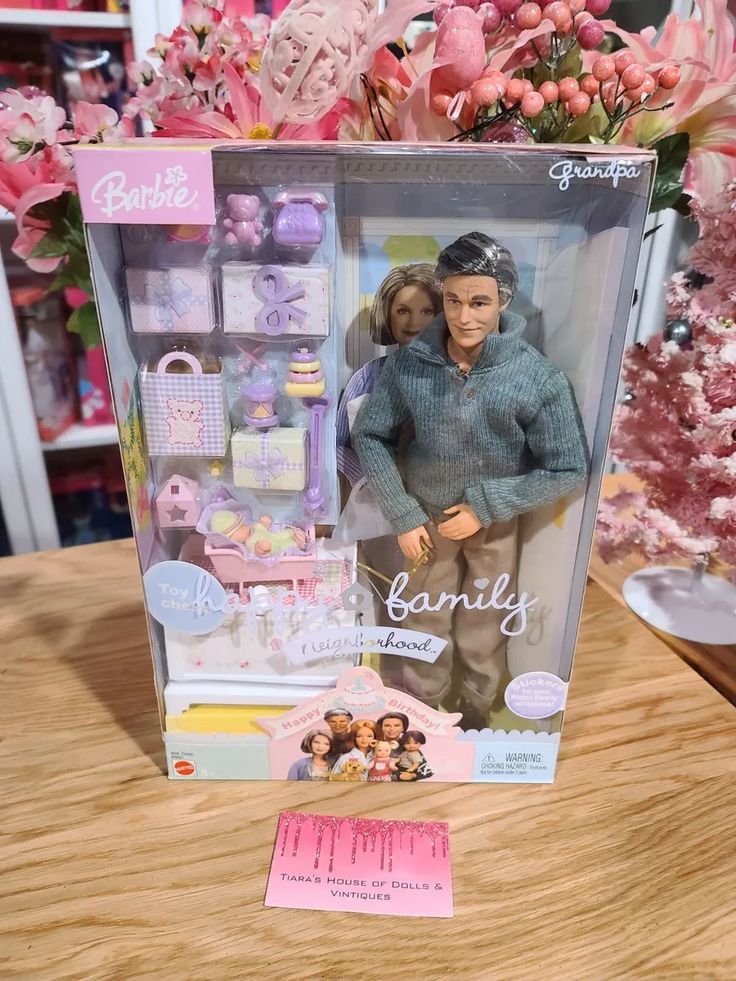 the doll is in its box on the table next to some flowers and other items