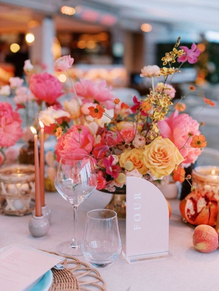 the table is set with pink and yellow flowers in vases, silverware, candles and napkins