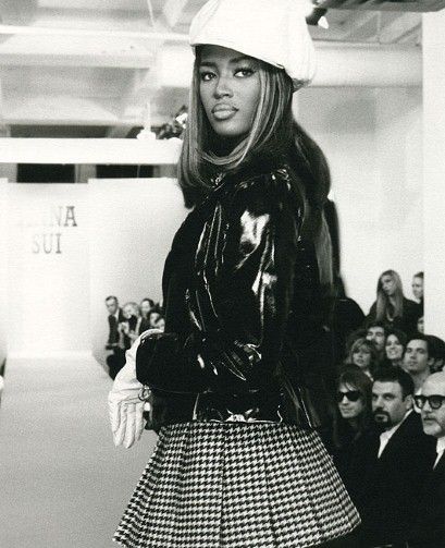 a black and white photo of a woman in a skirt on the runway with people watching