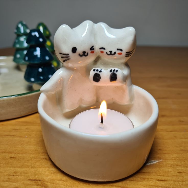 two white cats sitting in a bowl with a lit candle