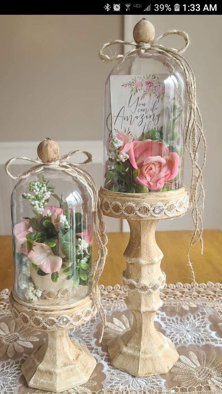 two glass jars with flowers inside sitting on a lace covered tableclothed table cloth