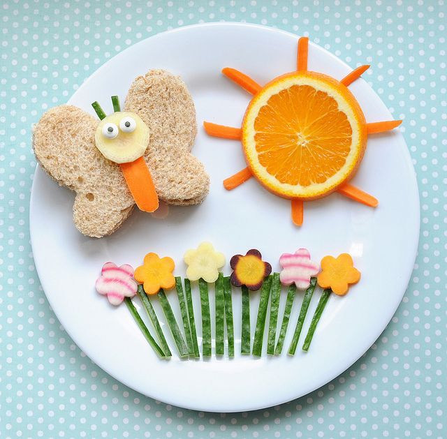 a plate with some food on it and an orange slice in the shape of a butterfly