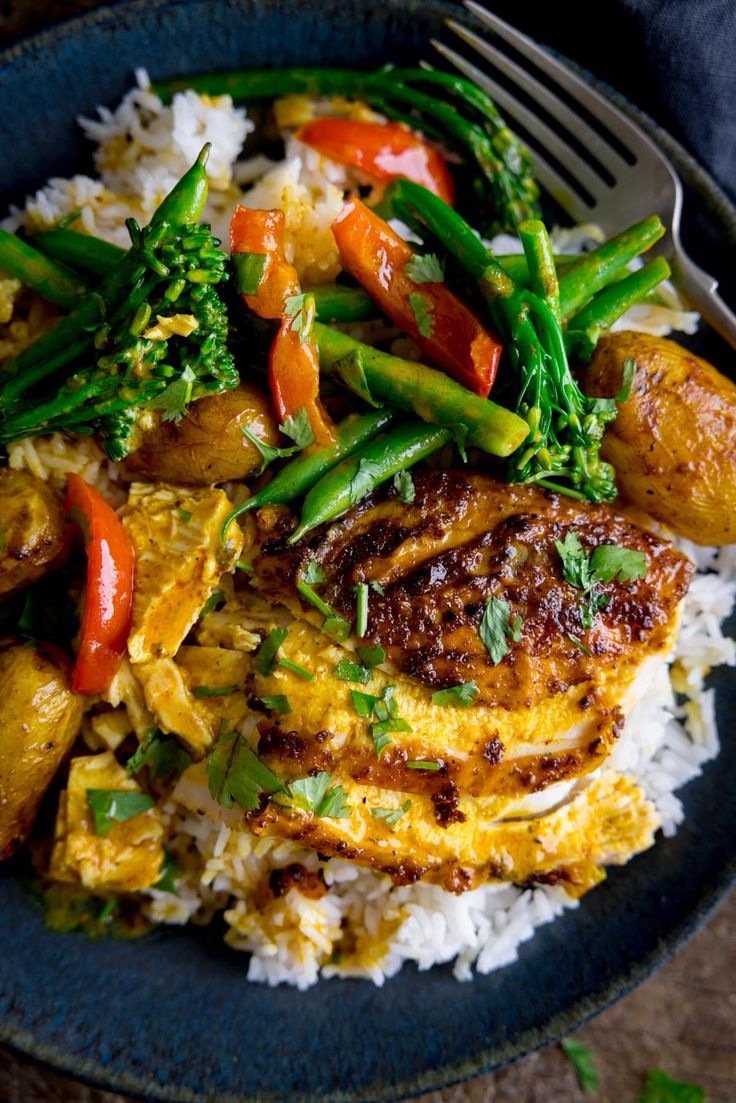 a blue plate topped with chicken and veggies on top of rice next to a fork