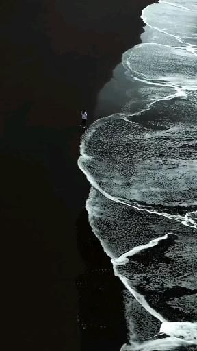 an aerial view of the ocean and beach with waves coming in to shore, as seen from above