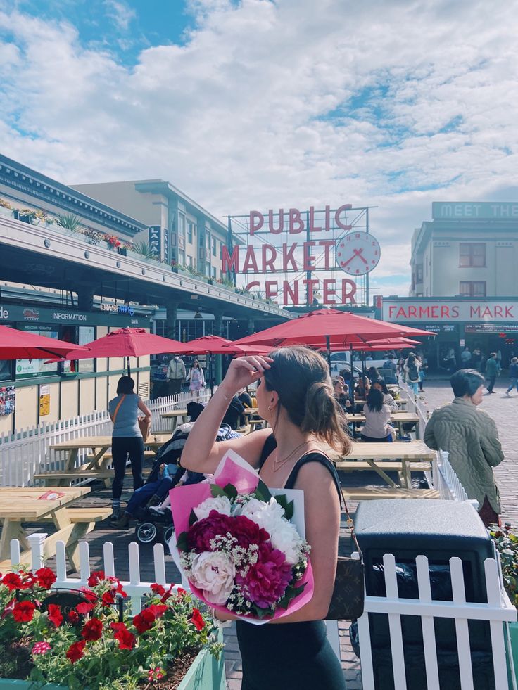 a woman standing in front of a market with flowers and umbrellas on the side