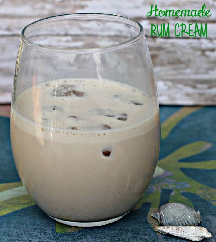 homemade rum cream in a glass on a blue tablecloth with shells and wood background